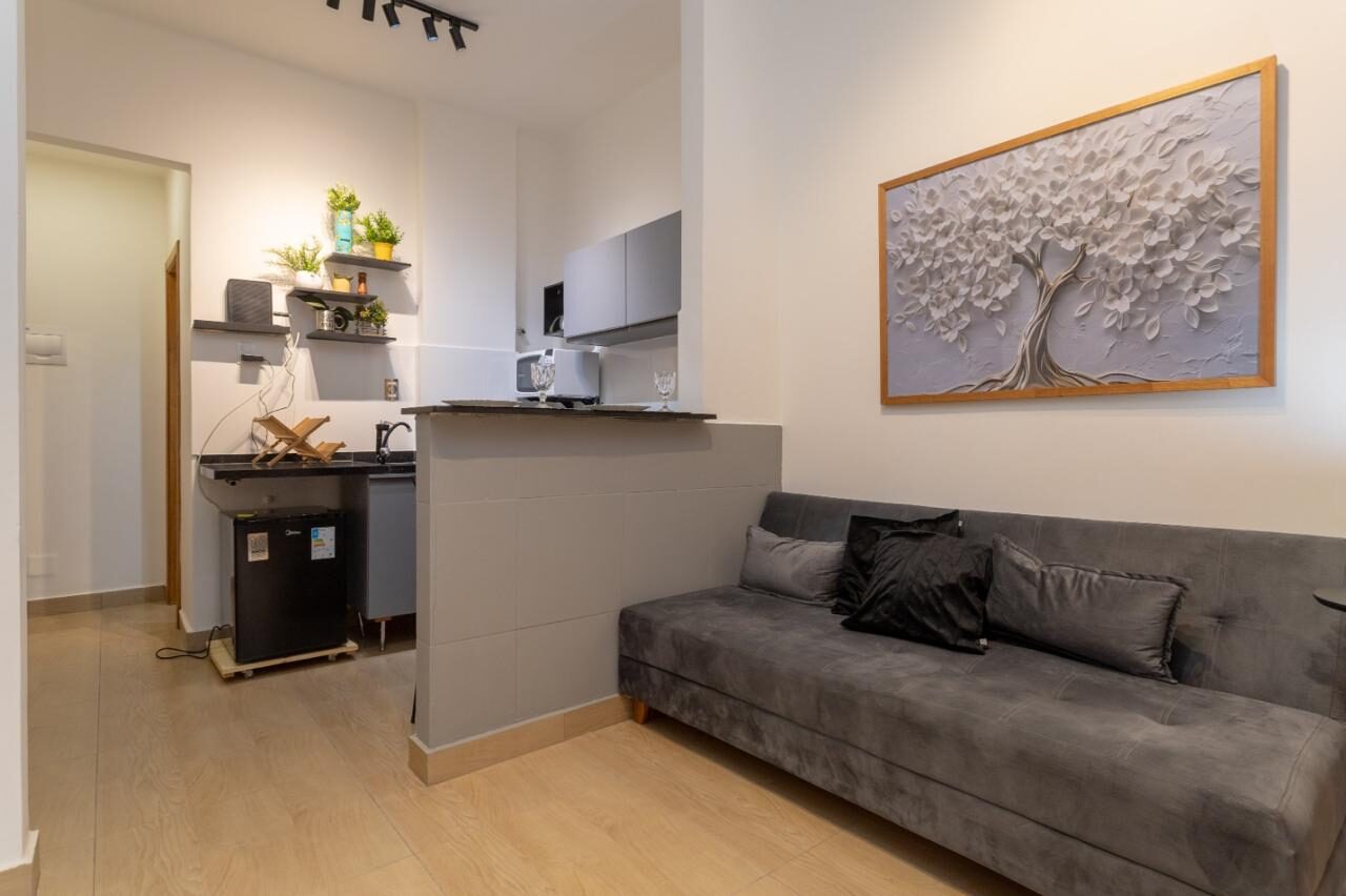 Sala e cozinha americana do estúdio em Copacabana, com sofá cinza e bancada preta