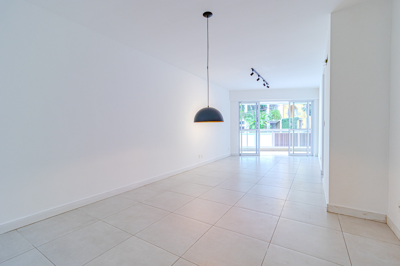 Sala vazia e iluminada do apartamento em Copacabana, Posto 4, com paredes brancas, piso claro e porta de vidro para a varanda