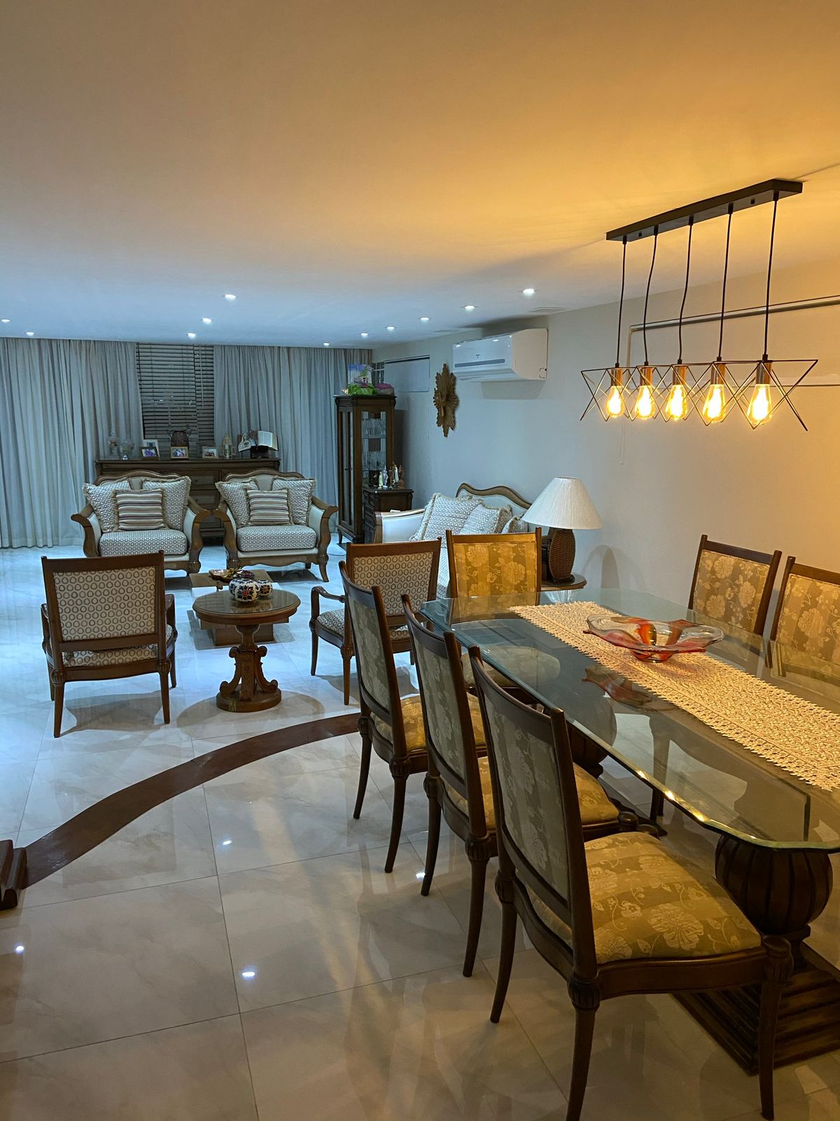 Sala de jantar e estar da casa de 5 suítes no Santa Mônica Jardins, com lustre de cinco lâmpadas, mesa de vidro e poltronas estofadas