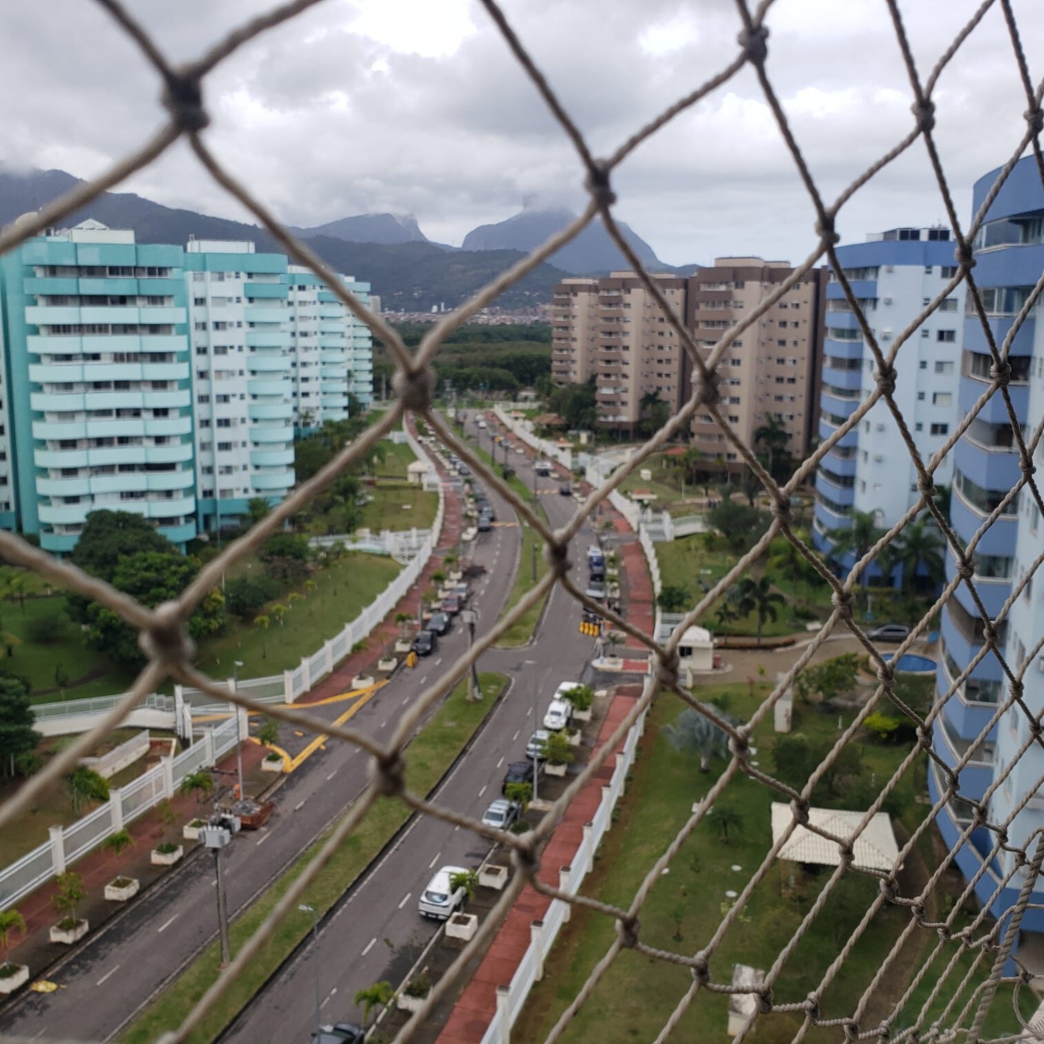 Vista da varanda do apartamento na Vila do Pan, com prédios do condomínio, ruas arborizadas e morros ao fundo